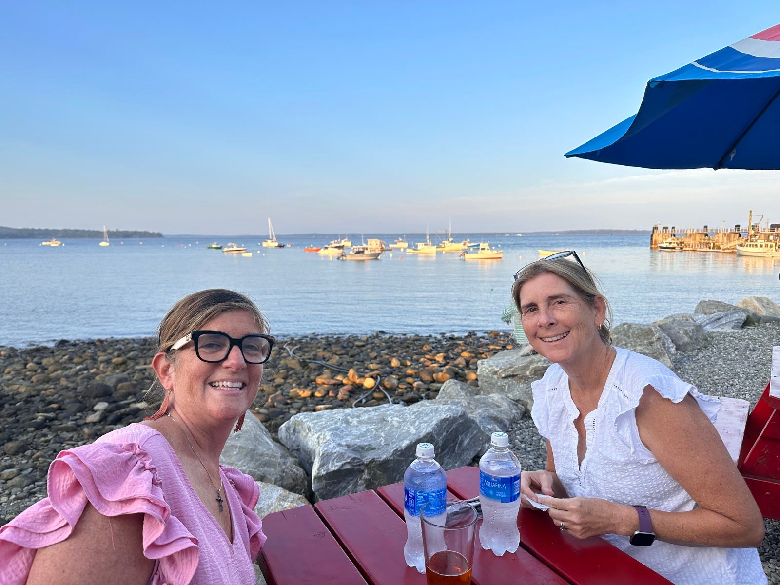 Two friends at a waterfront picnic table overlooking a Maine harbor