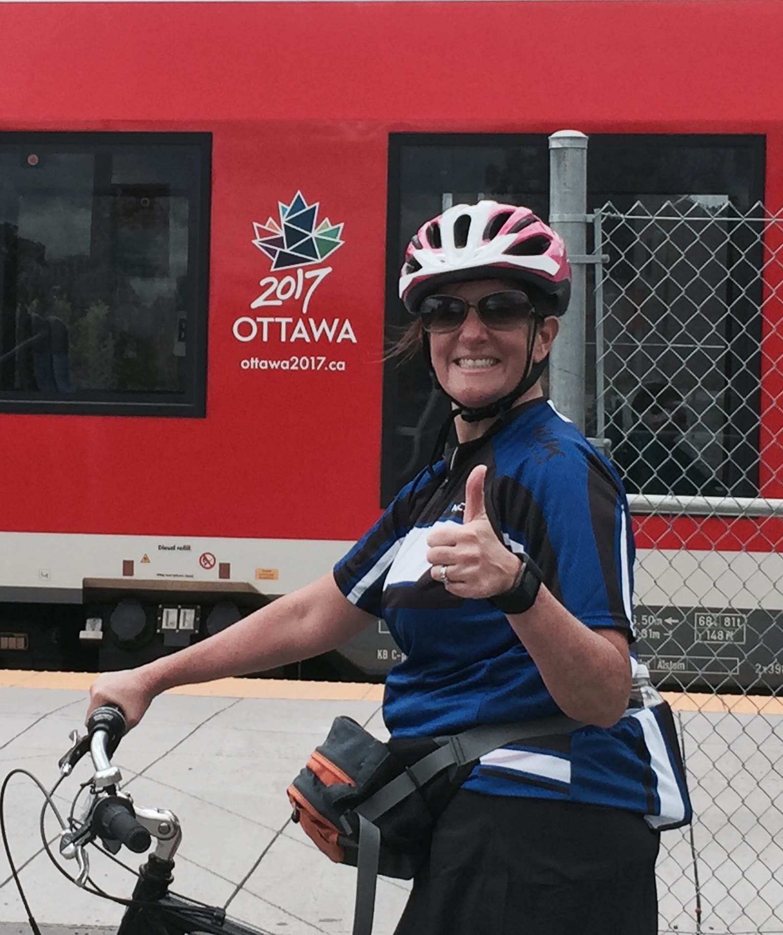 Leslie on a bike giving thumbs up by a red Ottawa train